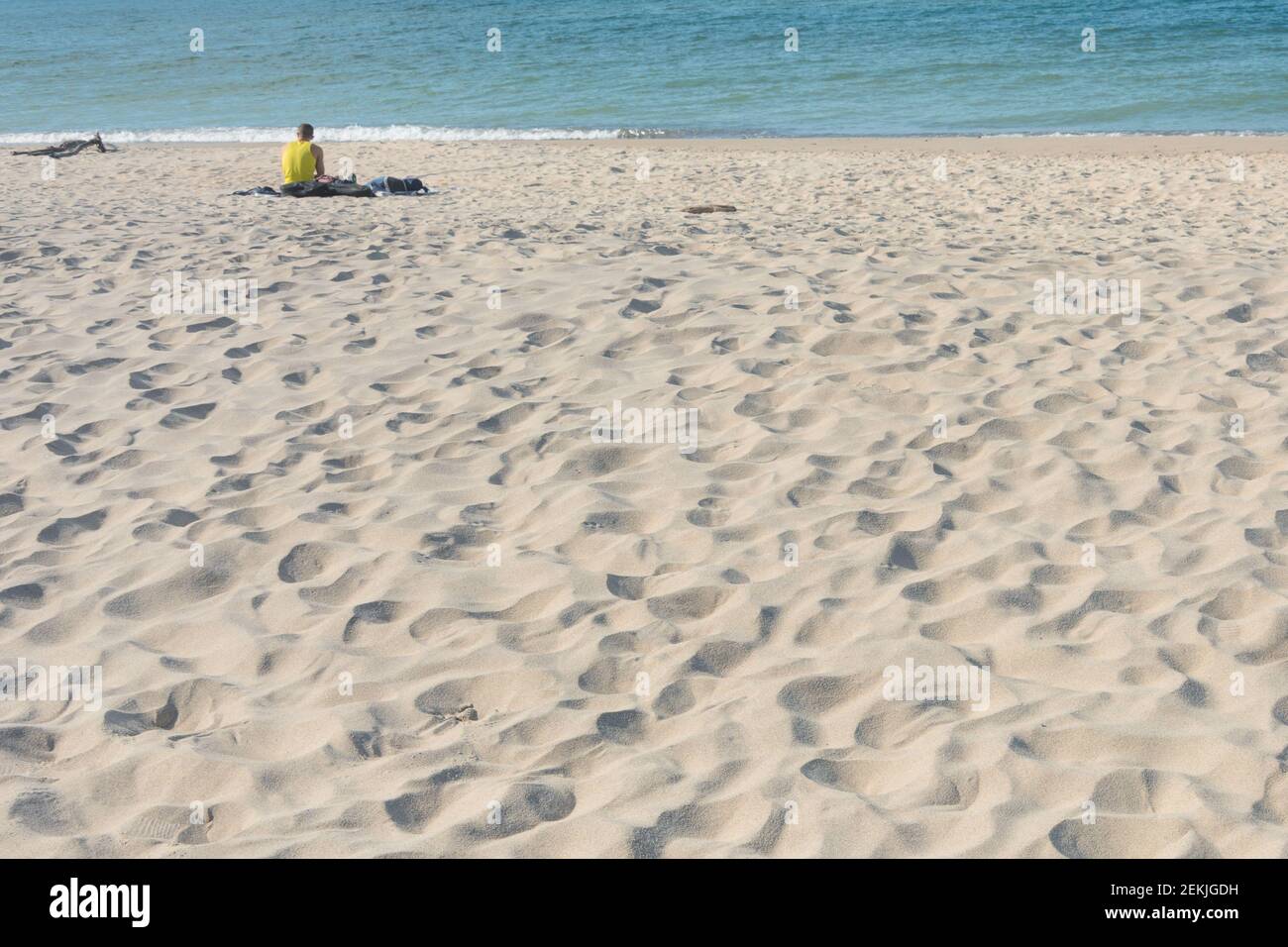 Weißer Sand am Strand. Silhouette eines Mannes, der am Ufer sitzt. Urlaub und Tourismus Konzept. Platz kopieren, Hintergrund verwischen, selektiver Fokus. Stockfoto