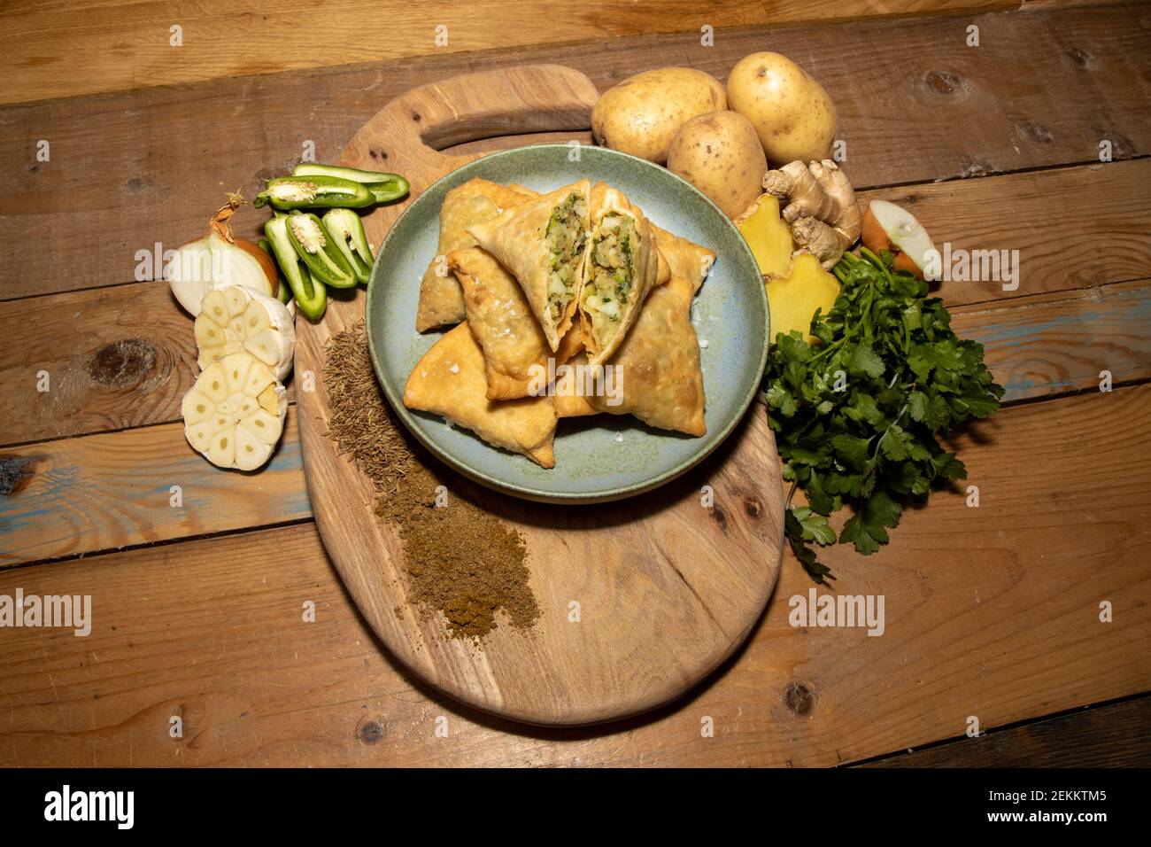 Ein köstlicher Stapel indischer Samosas auf einem hölzernen Küchentisch, umgeben von den Zutaten, die verwendet werden, um die leckeren Samosas zu kreieren. Stockfoto