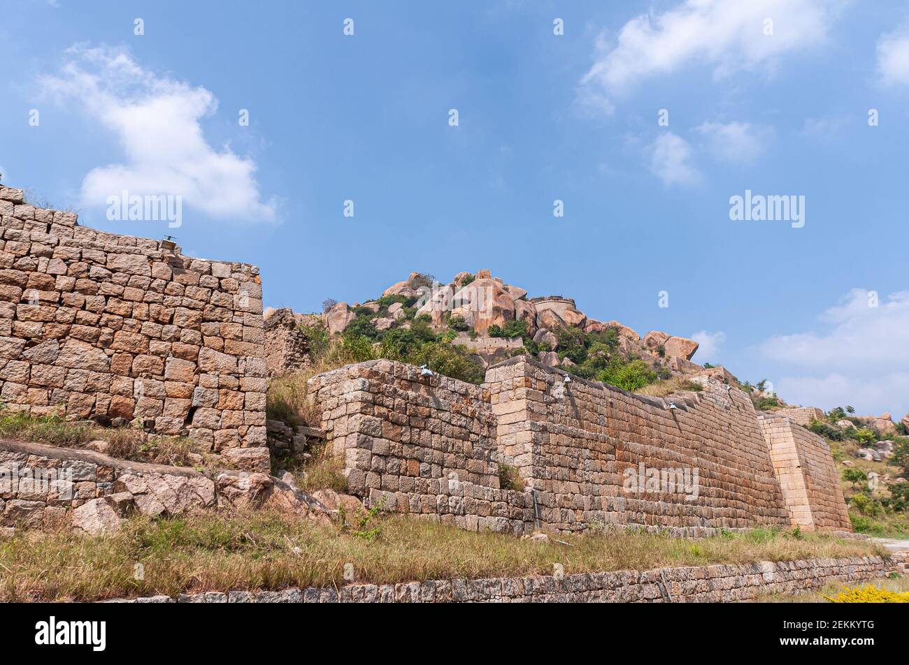 Chitradurga, Karnataka, Indien - 10. November 2013: Fort oder Elusuttina Kote. Braune Steinmauer unter blauer Wolkenlandschaft mit grüner Folliage und s Stockfoto