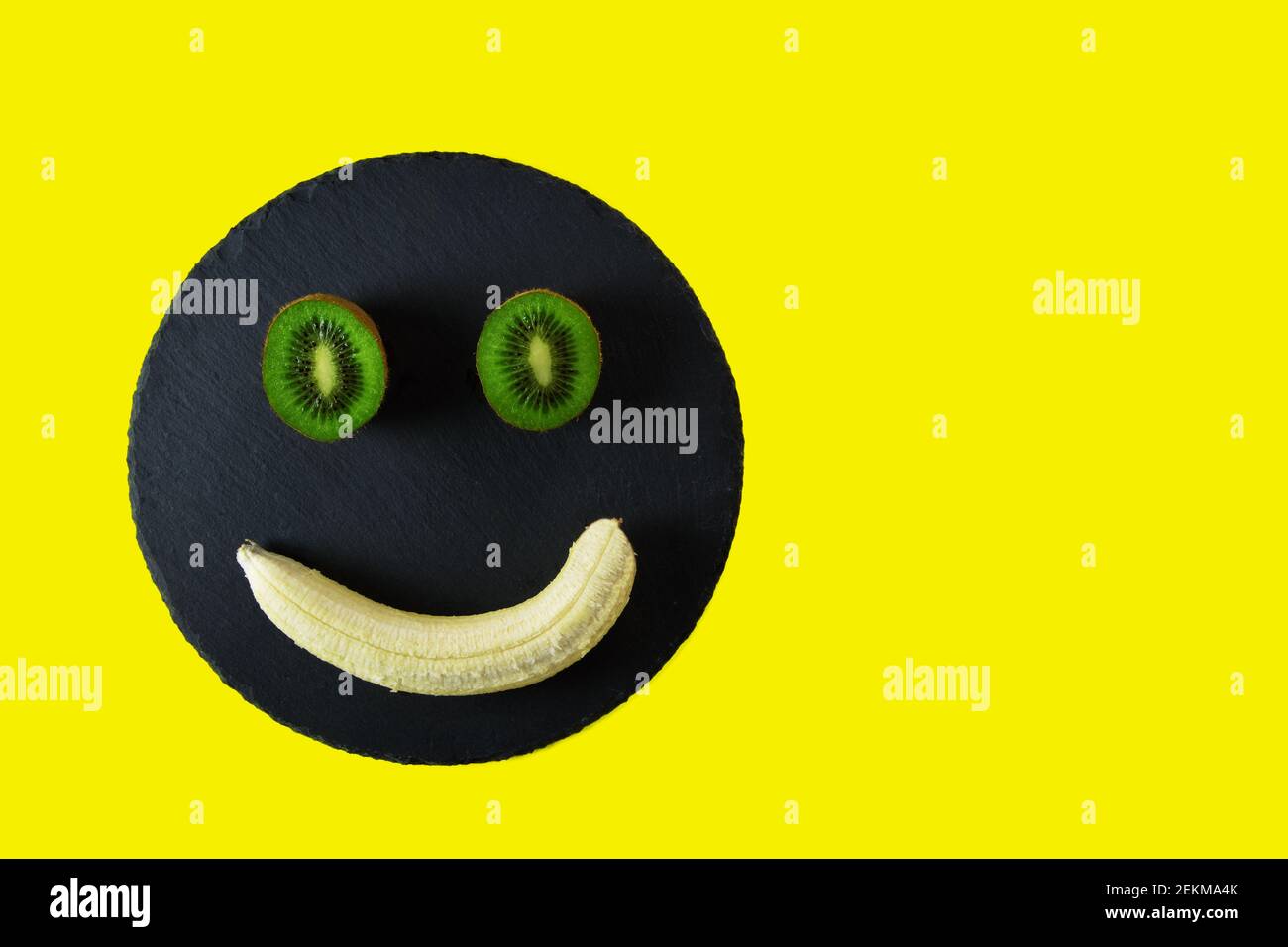 Kiwi Hälften und eine geschälte Banane auf schwarzem Tablett und Gelber Hintergrund Stockfoto