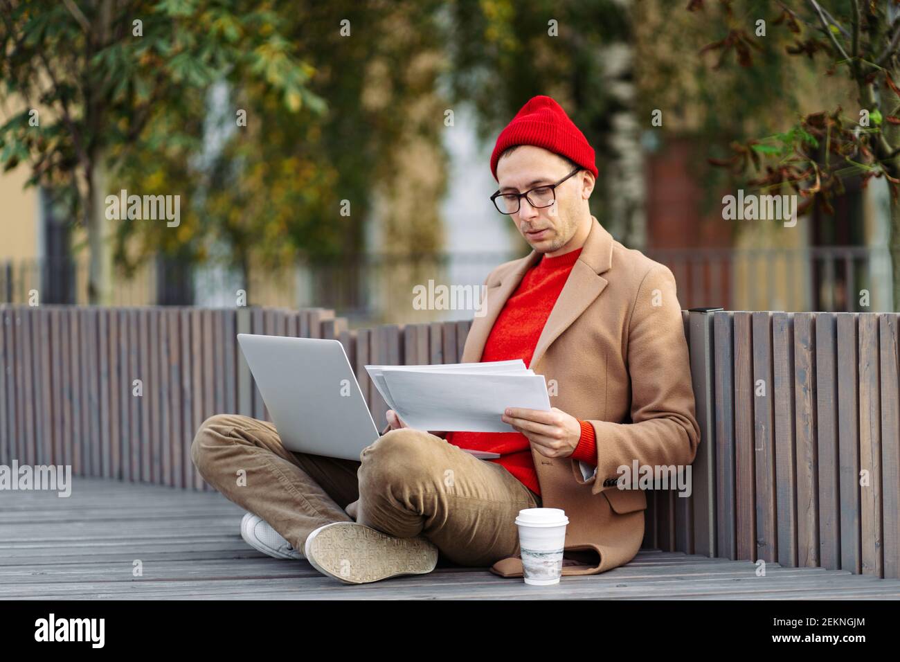 Serious Hipster Mann tragen Brille Lesen von Dokumenten, Remote-Arbeit mit Laptop, sitzen im Freien Stockfoto