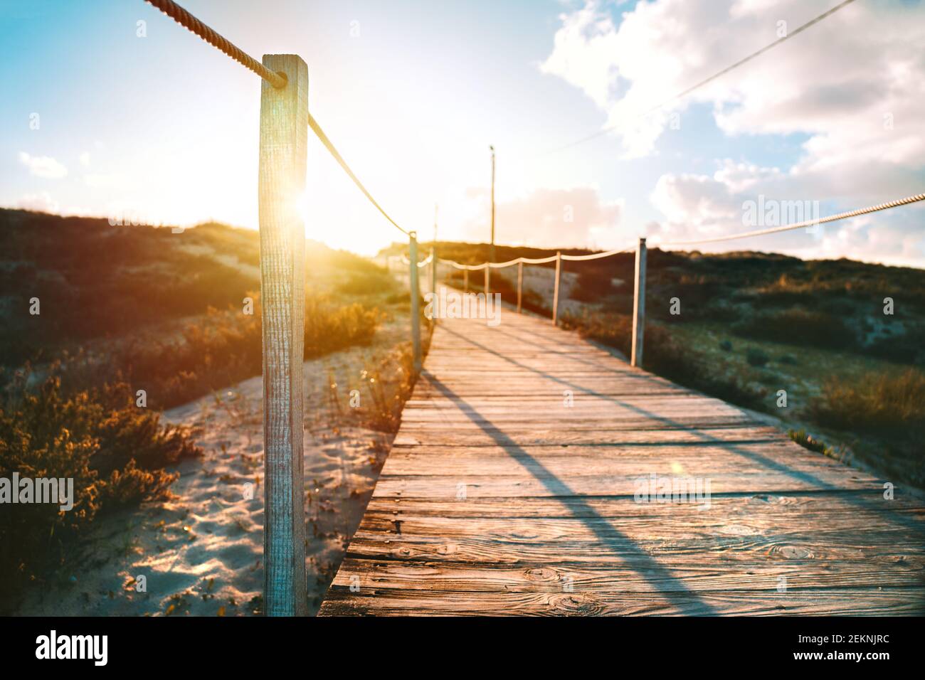 Holzweg zum Sandstrand und Meer mit hellen Sonnenstrahlen bei Sonnenuntergang oder Sonnenaufgang. Costa Da Caparica, Portugal Stockfoto