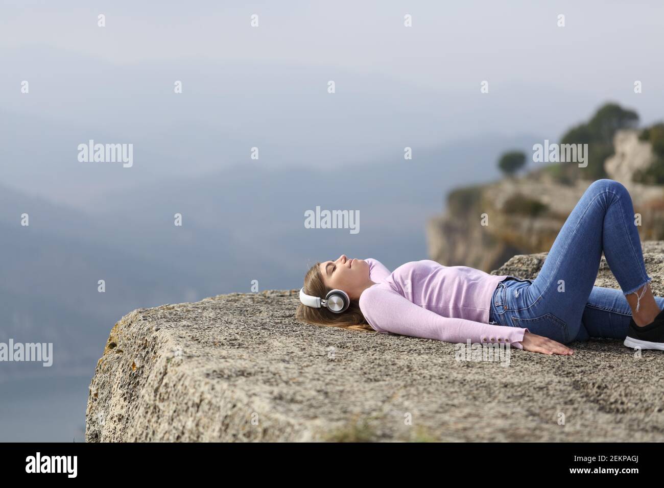 Glückliche Frau mit Kopfhörern, die Musik in einer Klippe hört In den Bergen Stockfoto