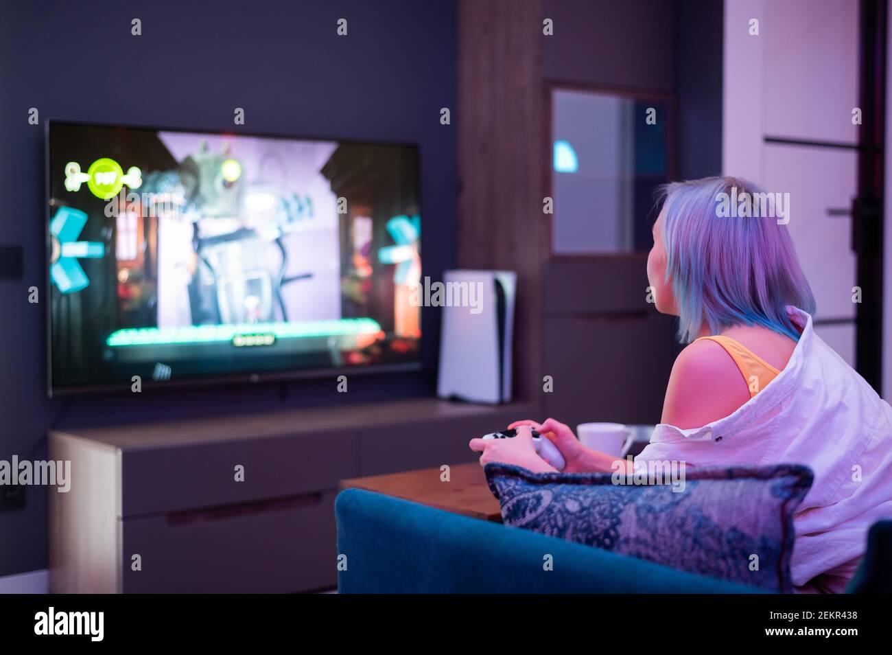 Schöne blauhaarige Mädchen hält Gaming-Contorller spielen Videospiele zu Hause. Rückansicht. Stockfoto