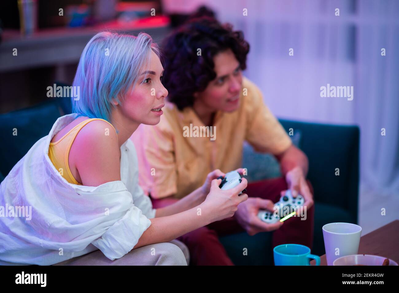 Schöne blauhaarige Mädchen und junge Kerl hält Gaming-Contorllers spielen Videospiele zu Hause. Stockfoto