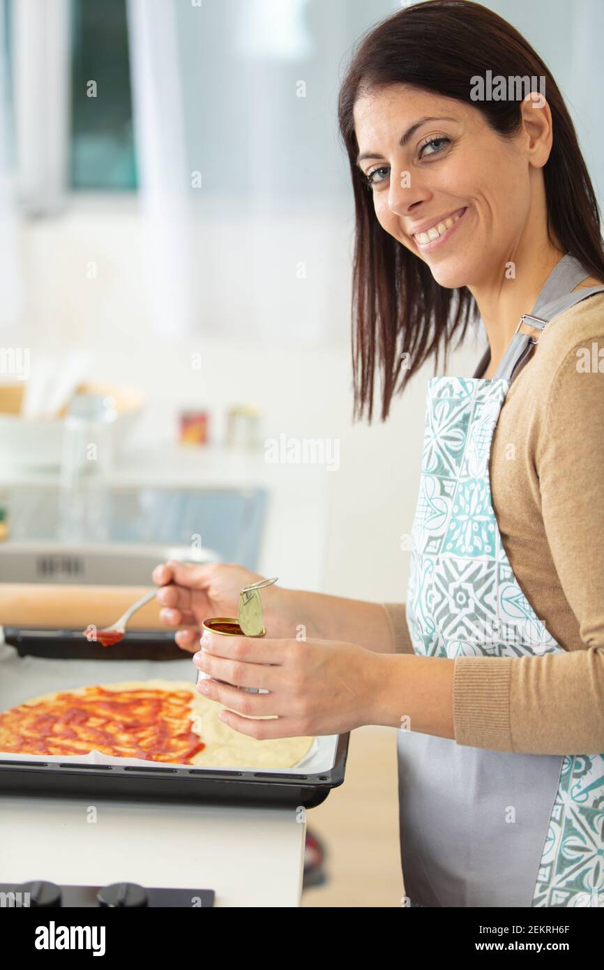 Frau, die Tomatensauce auf Pizza zugab Stockfoto