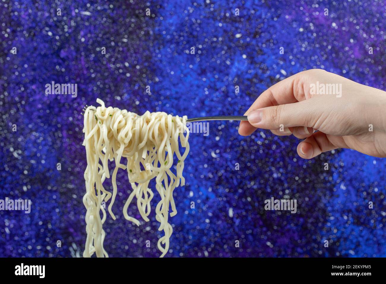 Weibliche Hand hält Gabel mit Nudeln auf blauem Hintergrund Stockfoto