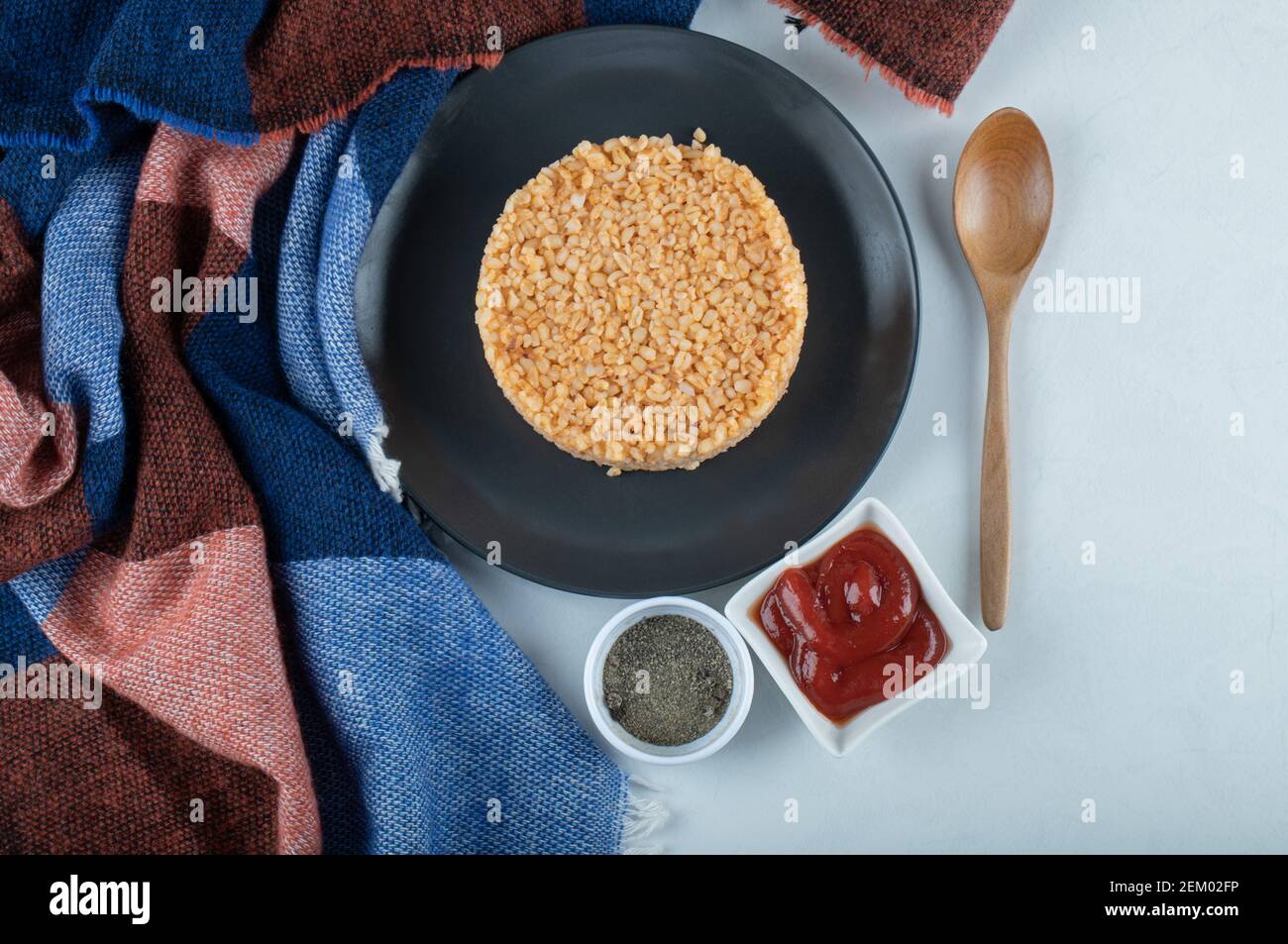 Ein dunkler Teller voller Bulgur mit Pfeffer und Ketchup Stockfoto