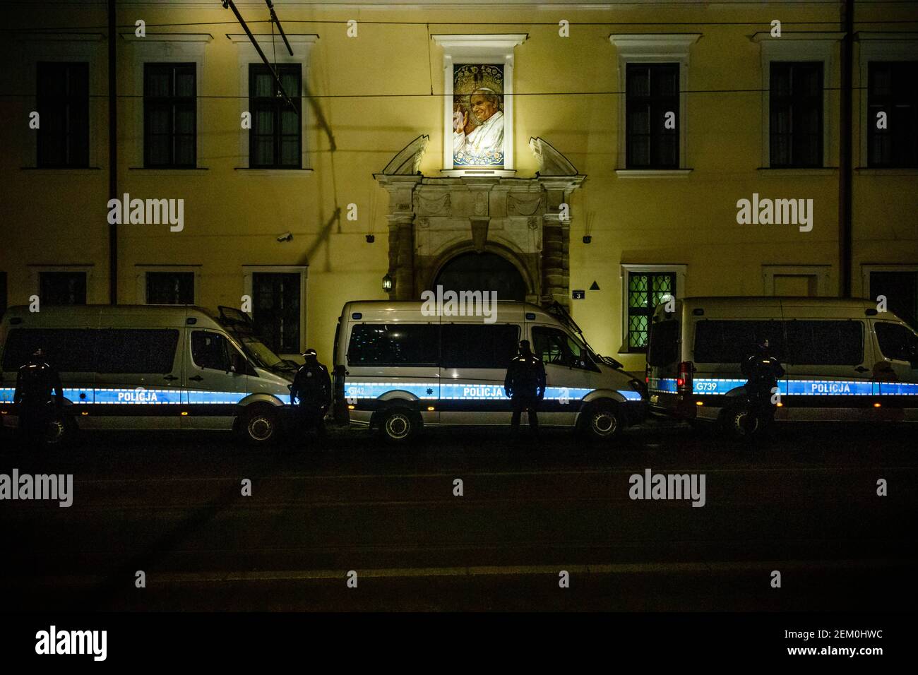 Eine Reihe von Polizeiwagen und Polizisten vor dem katholischen städtischen Kuriengebäude ist während der Demonstration zu sehen. Ein Bild von Johannes Paul II. Ist Stockfoto