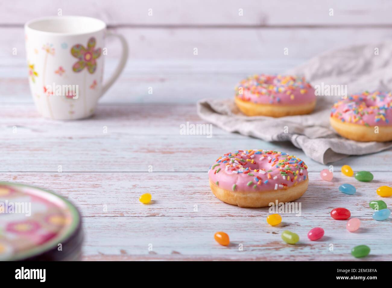 Leckere Donuts mit rosa Glasur, bunten Streuseln und Gelee-Bohnen auf Holzhintergrund. Süßes Gebäck als Snack für Kindergeburtstag. Stockfoto