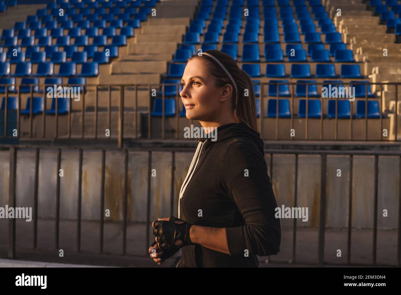 Junge Frau im schwarzen Sportanzug laufen in einem Stadion. Sonne im Gesicht. Stockfoto