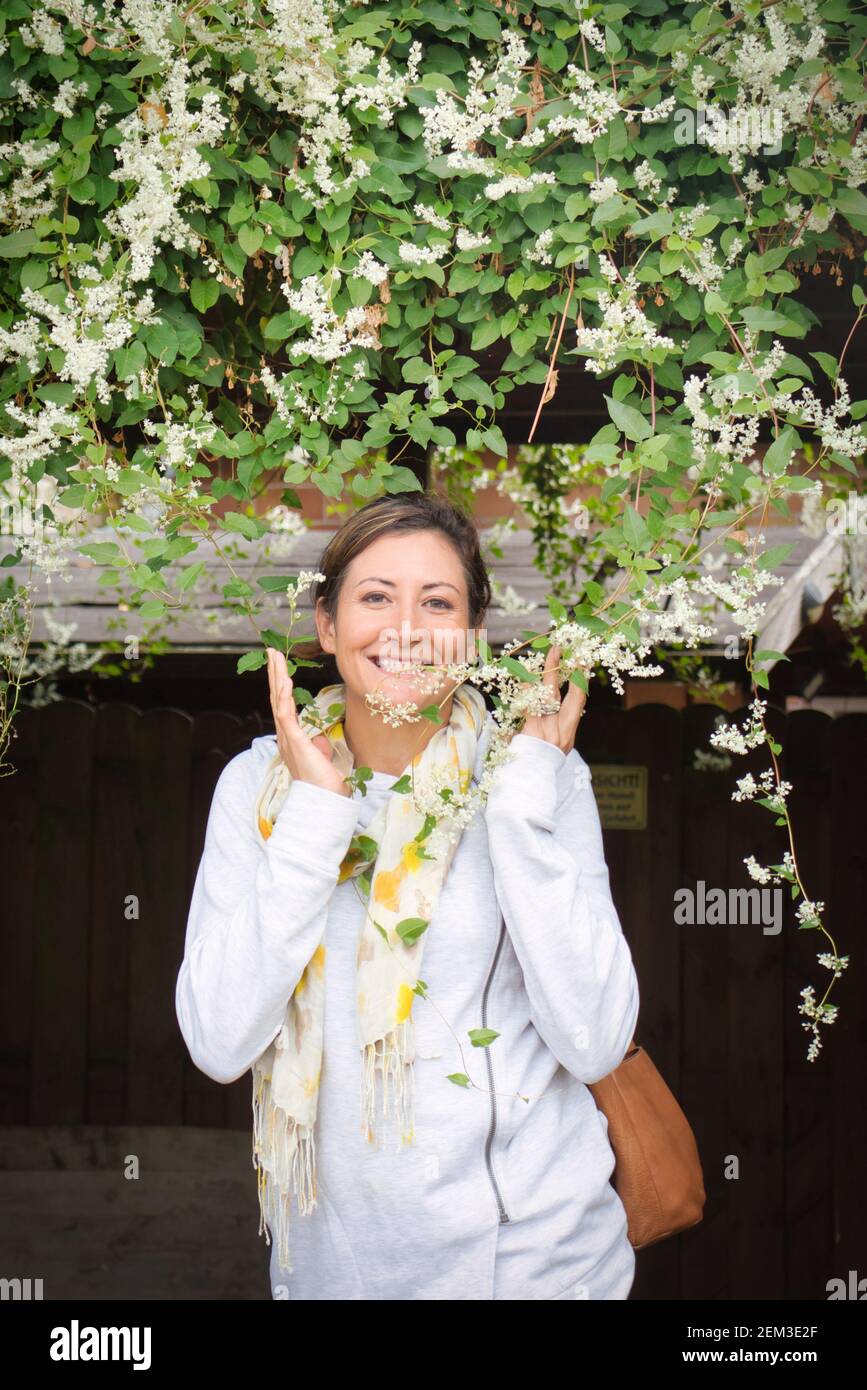 Amerikanische Ureinwohnerin, die unter weißen Blumen neben einem historischen Gebäude in Florsheim Dalsheim steht. Stockfoto