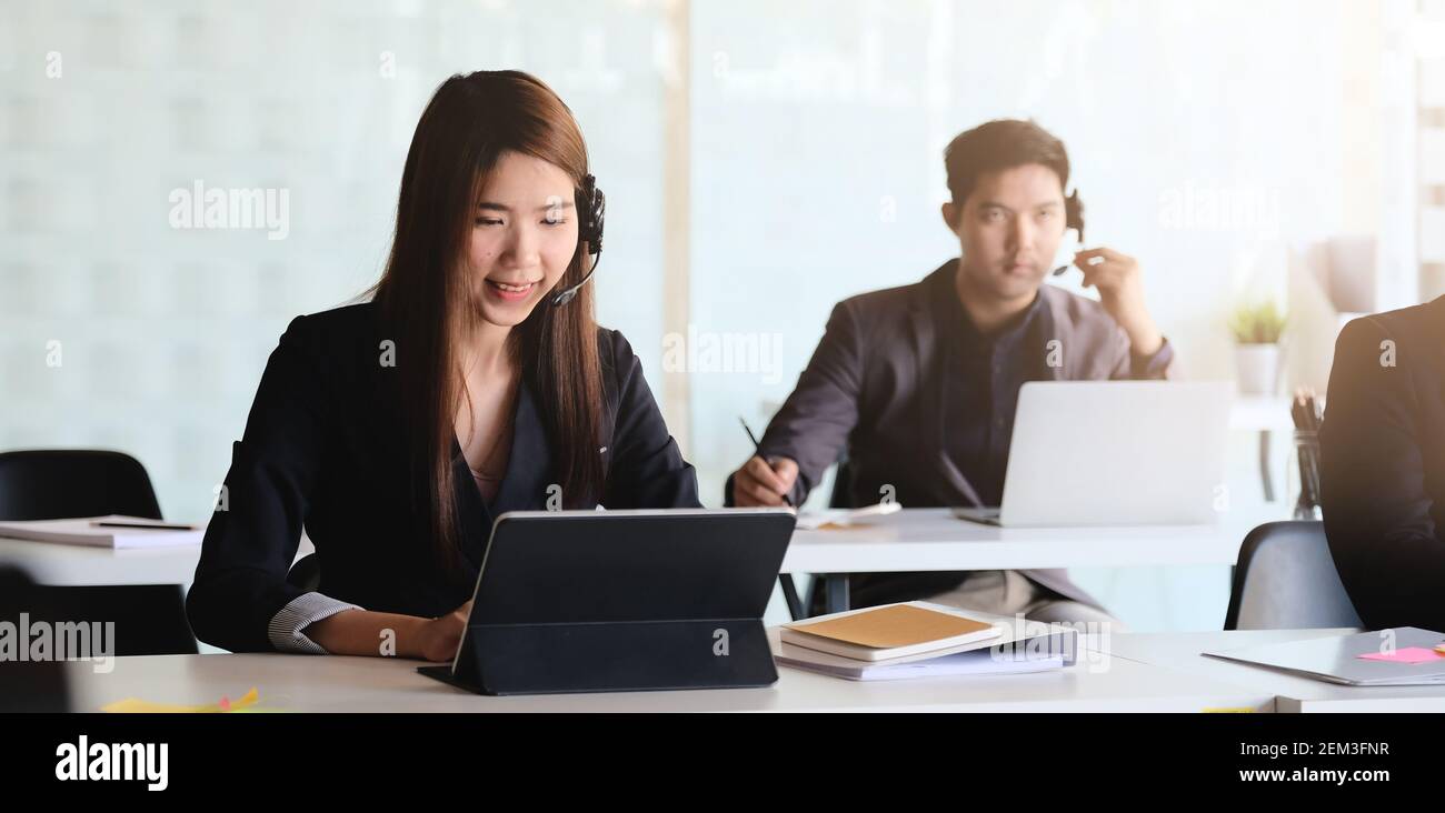 Junge asiatische Frau, die im Callcenter arbeitet, umgeben von Kollegen. Stockfoto