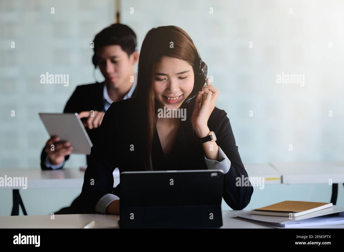 Junge asiatische Frau, die im Callcenter arbeitet, umgeben von Kollegen. Stockfoto