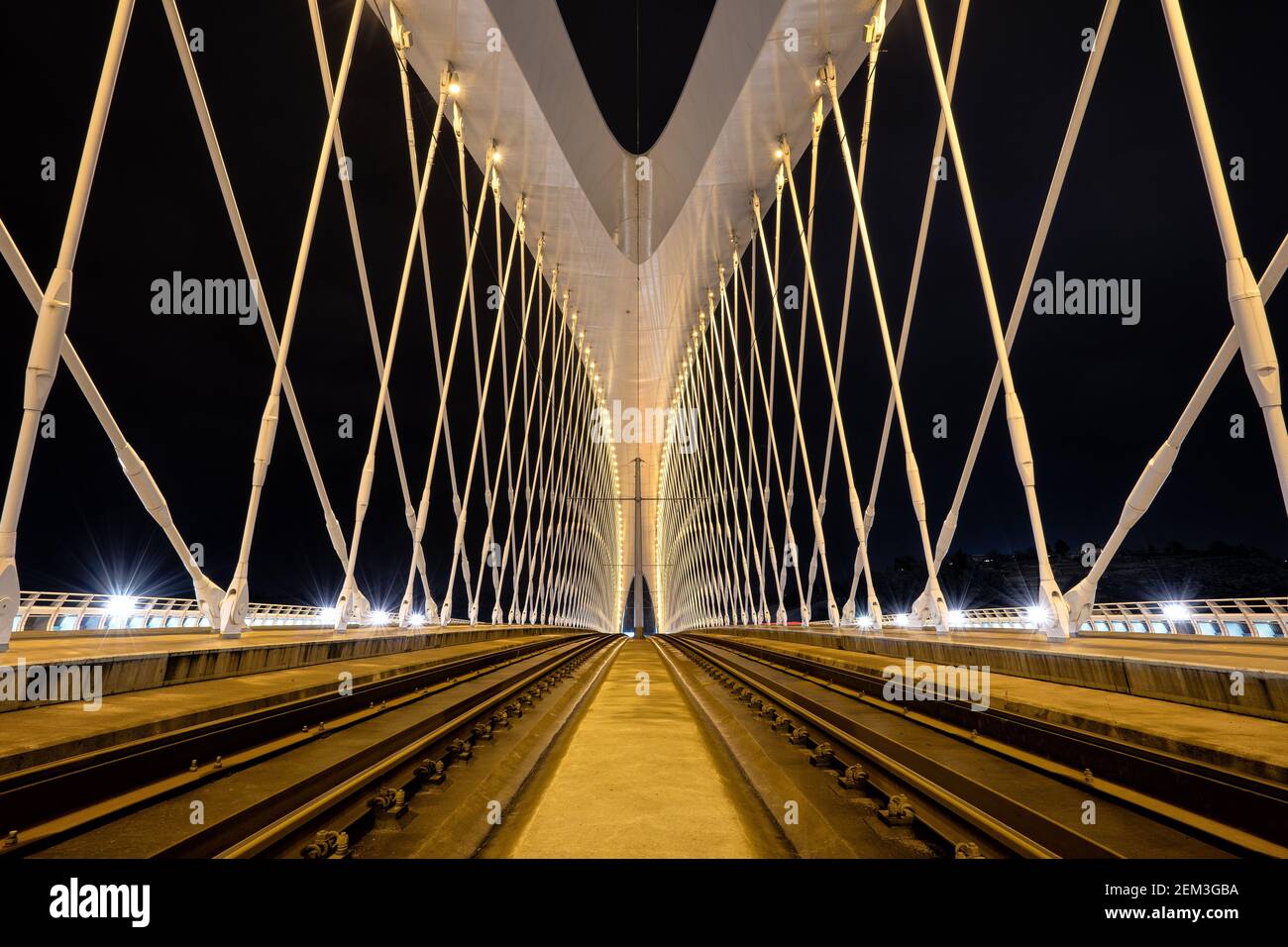 Symmetrischer Brückenbau in der Nacht mit hellen Lichtern, Vibratenfarben und Schienen in der Mitte. Stockfoto