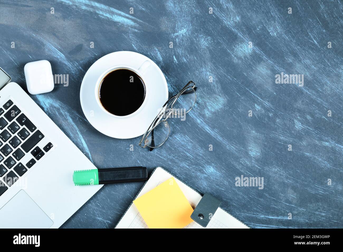 Eine Tasse Tee, Laptop, Notebook, Brille und Notizblöcke auf blauem Schreibtisch Stockfoto