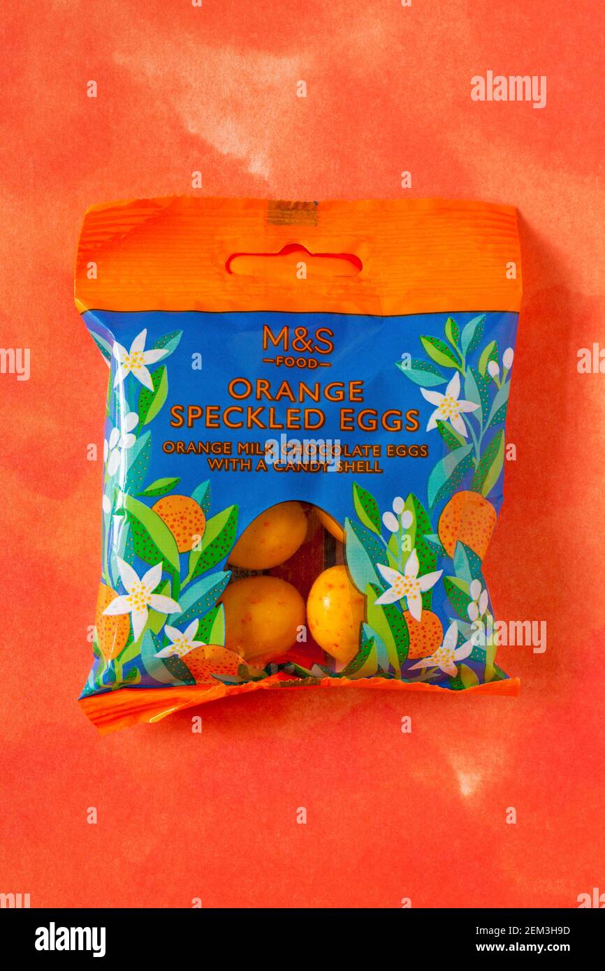 Paket mit M&S Orange gesprenkelten Eiern, Orangenmilch Schokolade Eier mit einer Süßigkeitenschale, isoliert auf gemustertem orangenen Hintergrund - bereit für Ostern Stockfoto