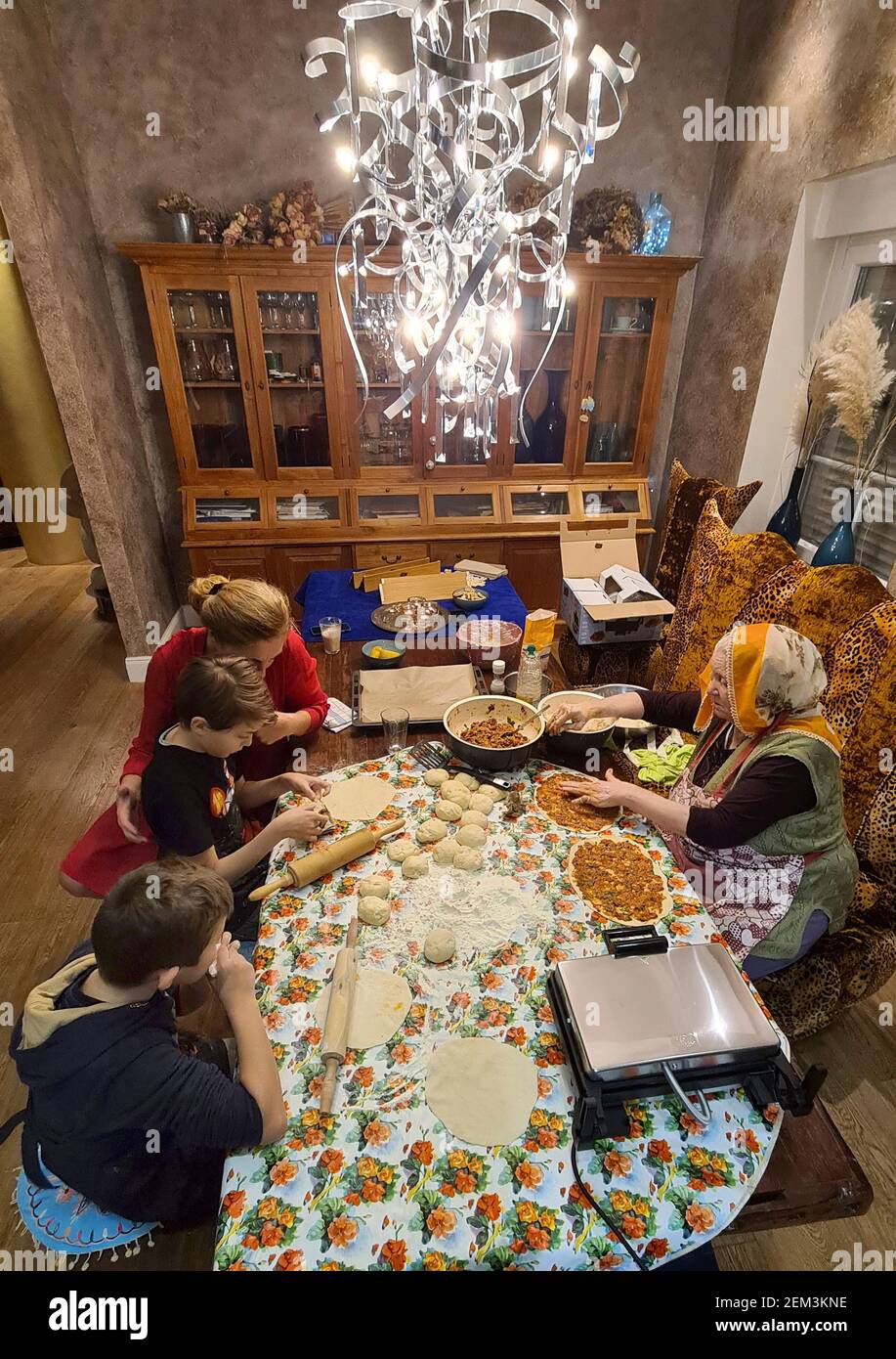 Großmutter beim Backen von Lahmacun mit Enkeln im Speisesaal, Mehrgenerationenbacken einer türkischen Familie, Deutschland Stockfoto