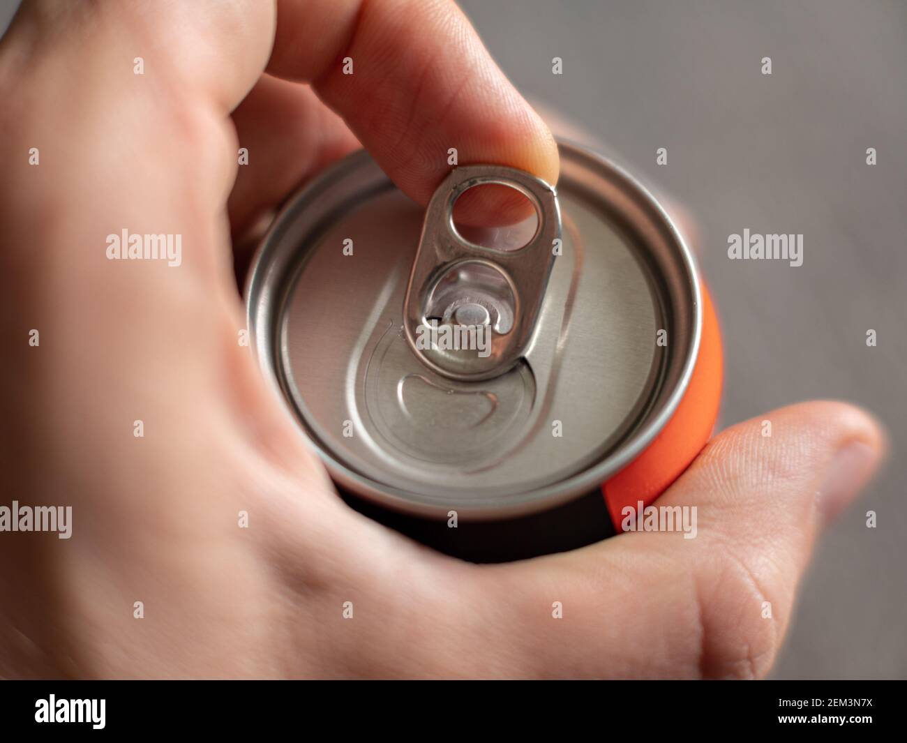 Ziehen der Lasche einer Aluminium-Getränkedose eines Energy Drink mit männlichen Händen auf neutralem Hintergrund Stockfoto