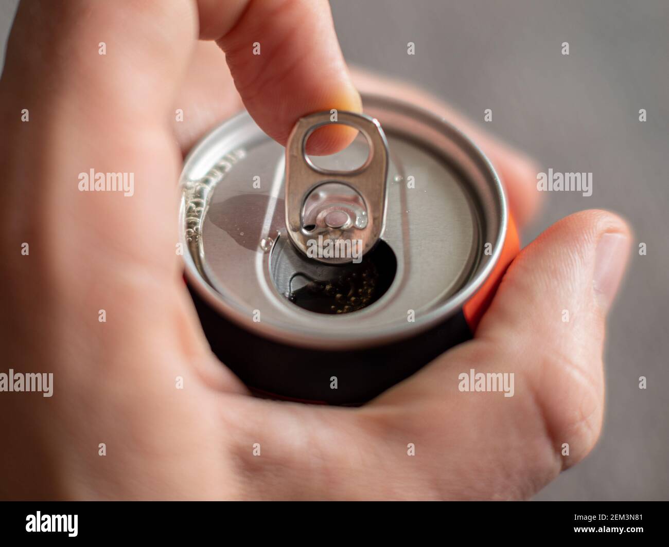 Ziehen der Lasche einer Aluminium-Getränkedose eines Energy Drink mit männlichen Händen auf neutralem Hintergrund Stockfoto