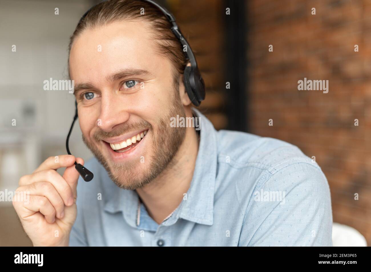 Schöner europäischer Mann mit Headset, das wegschaut und spricht, hat ein hellbraunes Haar, graue Augen und Bart, lächelnd freundlich, Telefonzentrale Stockfoto