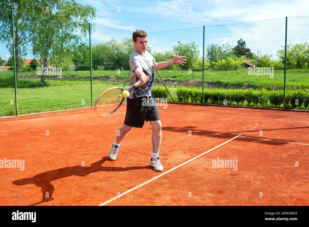 Junger Mann, der auf dem Sandplatz trainiert und Tennis spielt Stockfoto