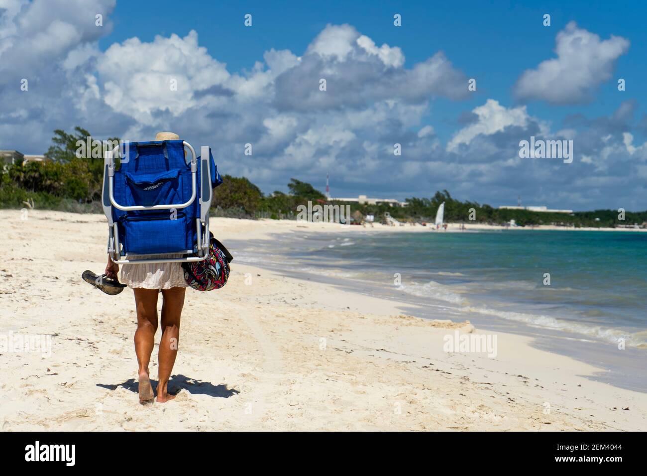 Touristische Spaziergänge am Karibischen Meer mit seinem Liegestuhl auf den Schultern in Mexiko. Im Hintergrund die Küste und der wolkige Himmel. Urlaubsreise CO Stockfoto