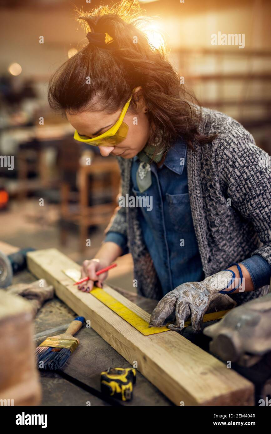 Nahaufnahme der fleißige konzentrierte professionelle ernsthafte Schreiner Frau Halten Lineal und Bleistift, während Marken auf dem Holz Am Tisch im Stockfoto