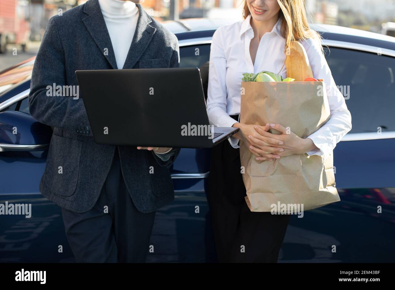 Nahaufnahme von beschnittenen Vorderansicht von geschäftigen modernen Menschen, Mann und Frau, die am Laptop-pc arbeiten, während sie sich auf dem modernen Auto auf öffentlichen Parkplätzen in der Nähe des Handels stützen Stockfoto