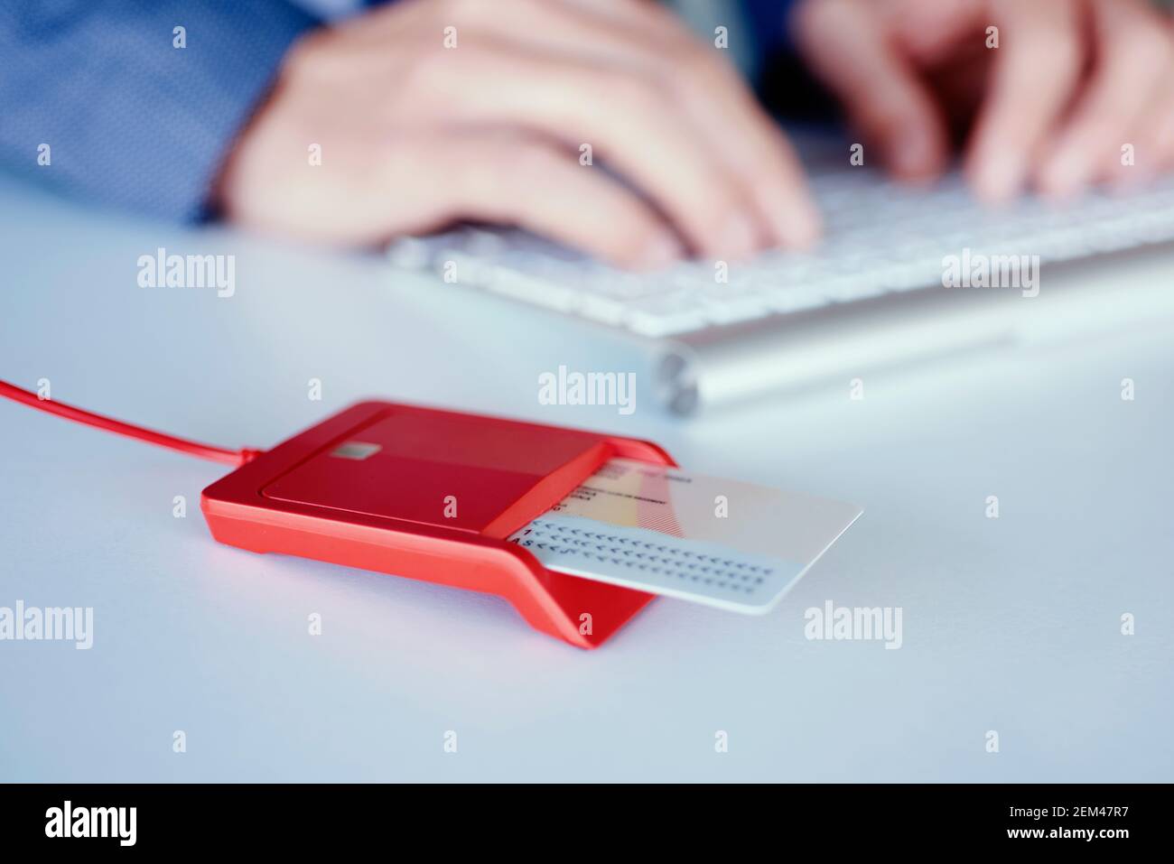 Nahaufnahme eines elektronischen Ausweises in einem roten Leser an der Rezeption und eines jungen kaukasischen Mannes, der einen eleganten blauen Anzug am Schreibtisch trägt Stockfoto