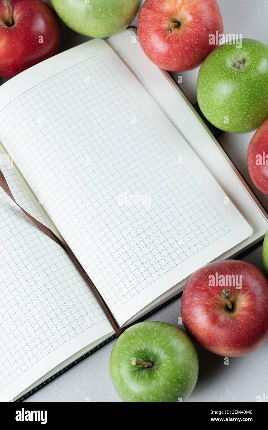 Grüne, rote Äpfel und ein leeres Rezeptbuch auf dem Tisch Stockfoto