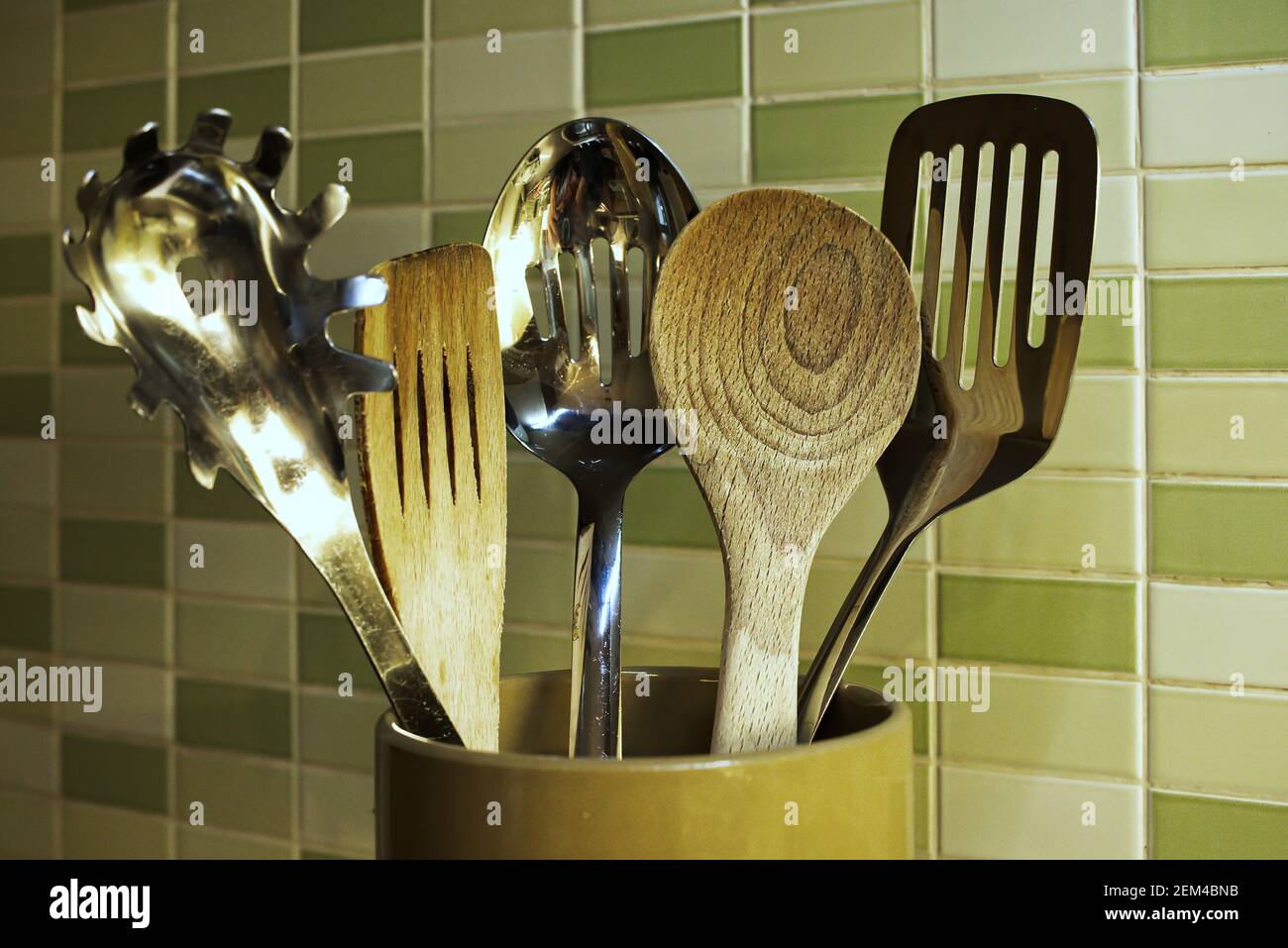Küchengeräte in einem Keramiktopf - Holzlöffel, Spachtel und Edelstahl-Werkzeuge zum Kochen von Speisen verwendet Stockfoto
