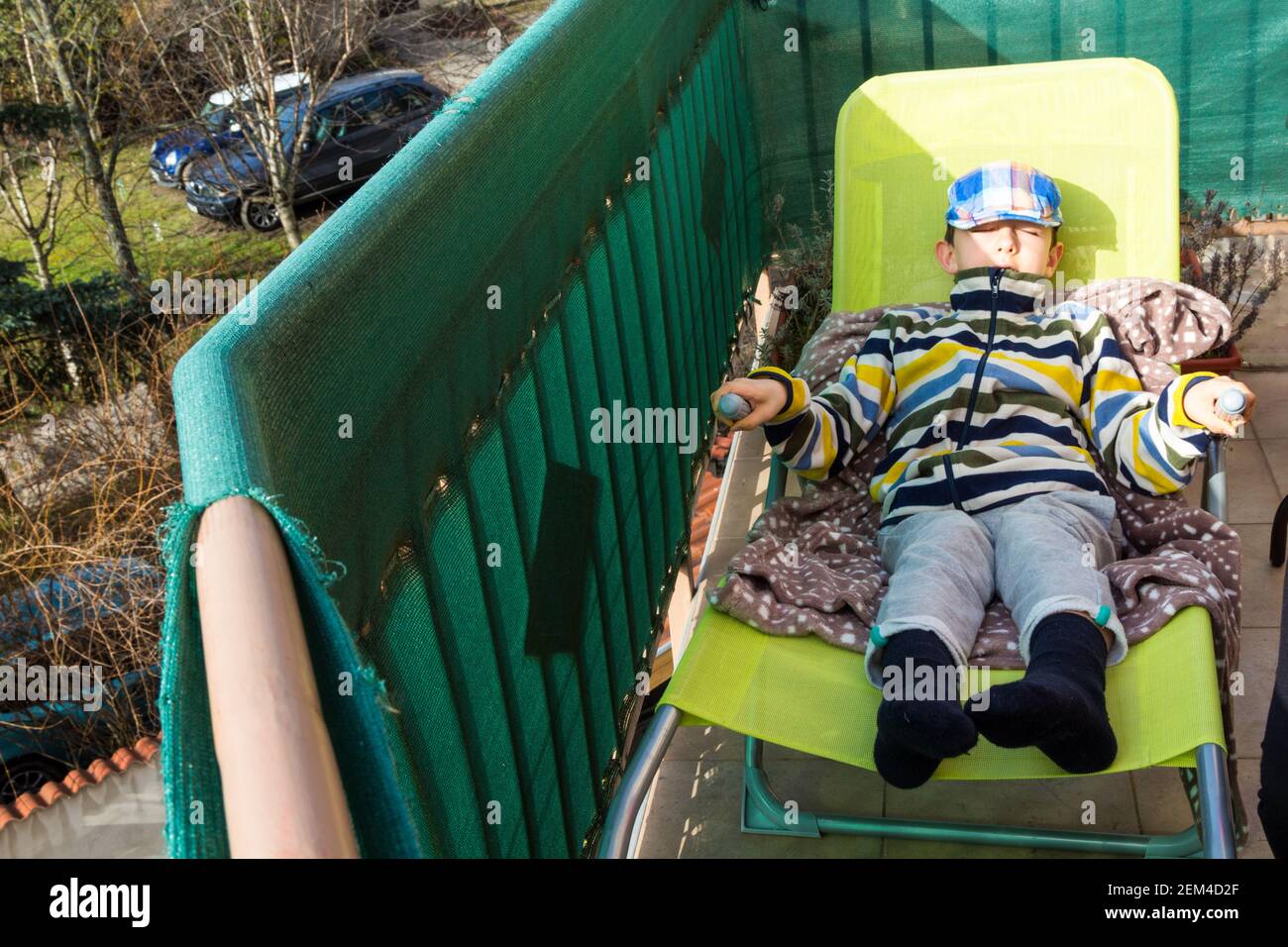Knabenkind liegt auf Liegestuhl in der milden Februarsonne während covid-19 Hausquarantäne, Sopron, Ungarn Stockfoto
