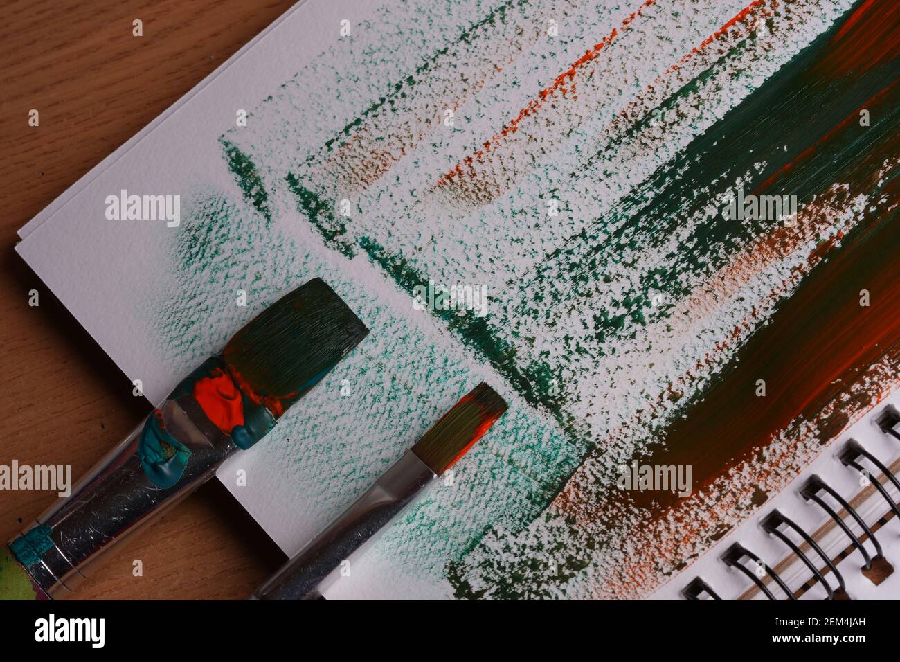 Zwei Pinsel, Papier, orange und grüne Farbstriche auf Papier gemischt, close-up Stockfoto