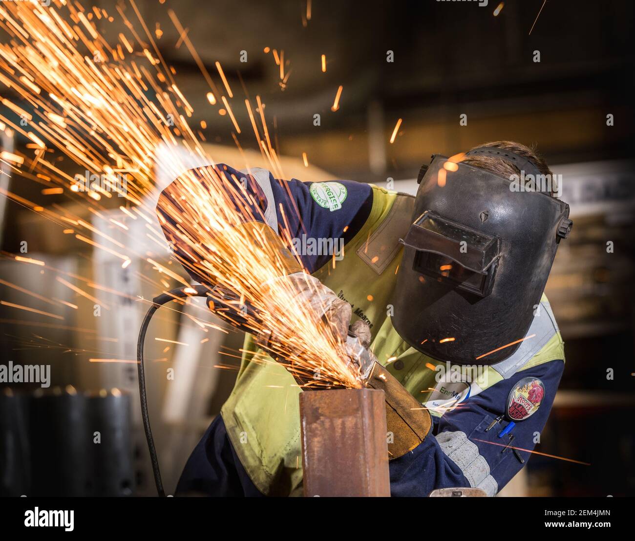 Ein Arbeiter mit Stulpen und einer Maske mit einem Schleifer Auf einem Stück Metall Stockfoto