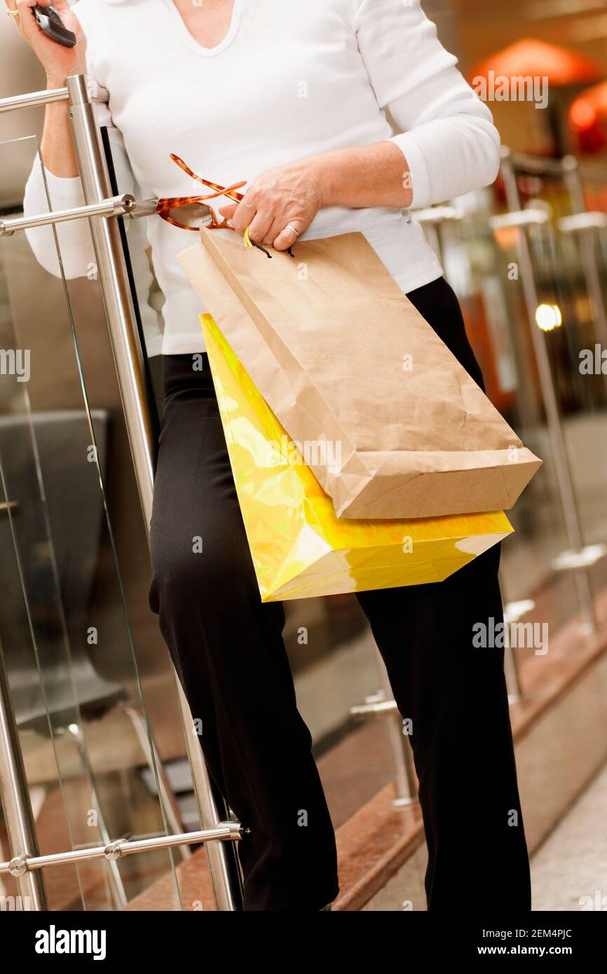 Nahaufnahme einer Frau mit einem Handy und Sonnenbrille mit Einkaufstüten Stockfoto