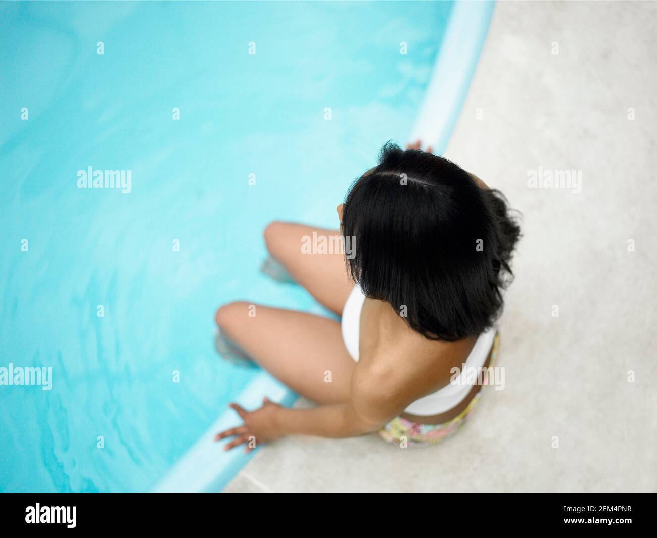 Blick auf eine Frau, die am Pool sitzt Mit ihren Beinen im Wasser Stockfoto