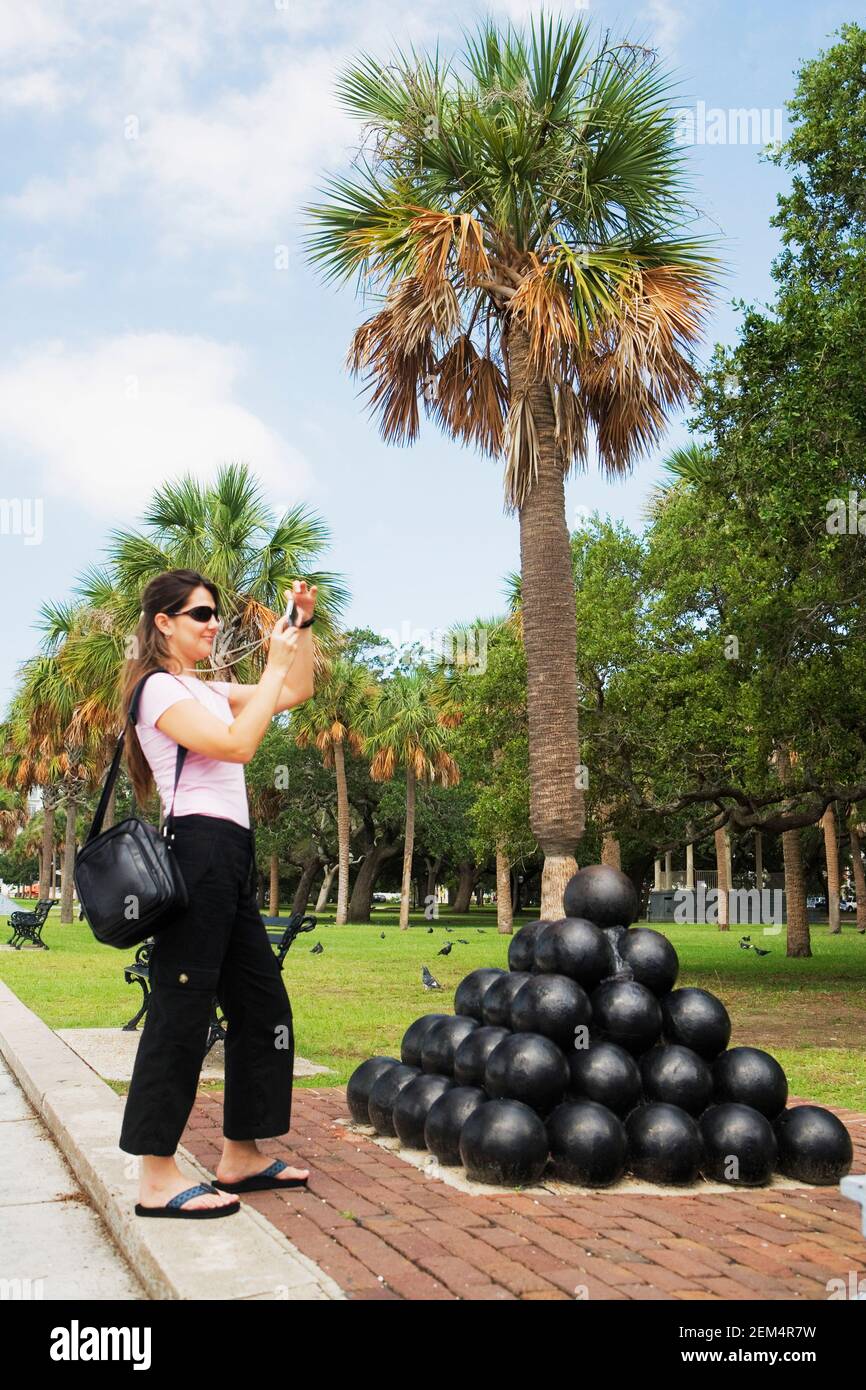 Seitenprofil einer mittleren erwachsenen Frau, die ein Foto gemacht hat Vor einem Haufen Kanonenkugeln Stockfoto