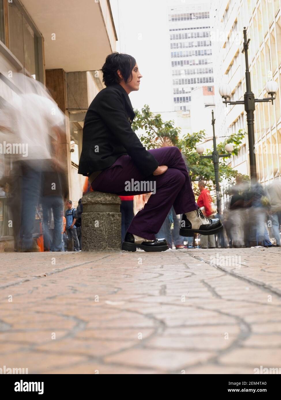 Seitenprofil eines jungen Mannes, der auf einem Gehweg sitzt Stockfoto