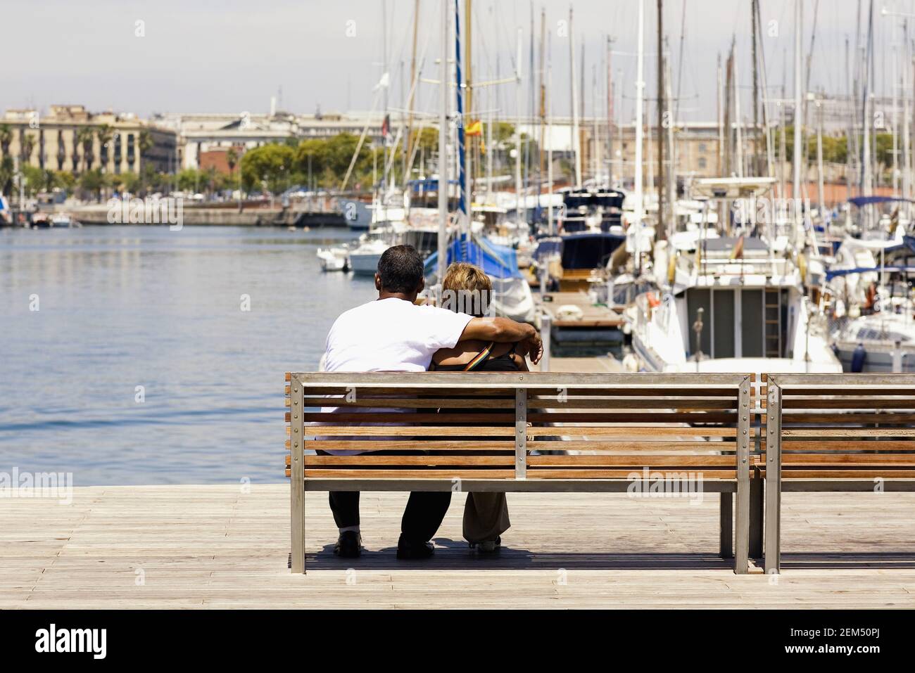 Rückansicht von zwei Personen, die auf einer Bank an einem Hafen sitzen, Barcelona, Spanien Stockfoto