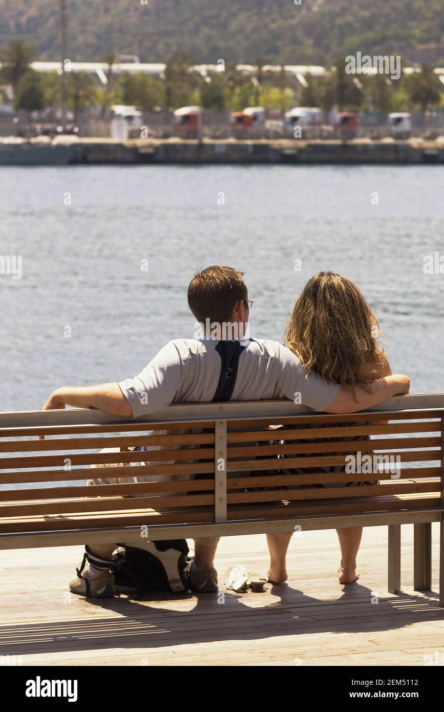 Rückansicht eines Mannes und einer Frau, die auf einer Bank am Flussufer sitzen, Barcelona, Spanien Stockfoto