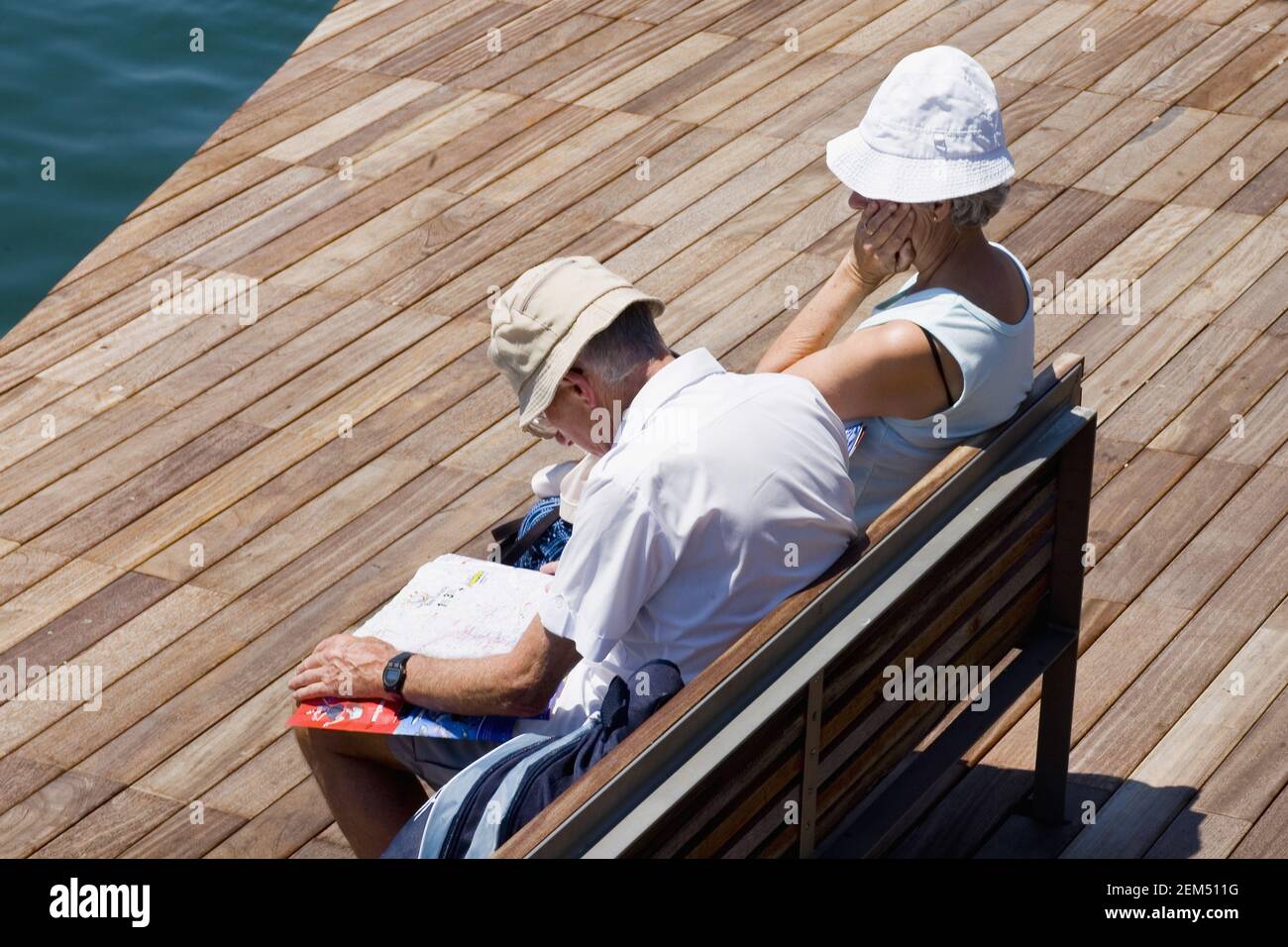 Blick auf ein Seniorenpaar, das auf einer Bank am Flussufer sitzt, Barcelona, Spanien Stockfoto