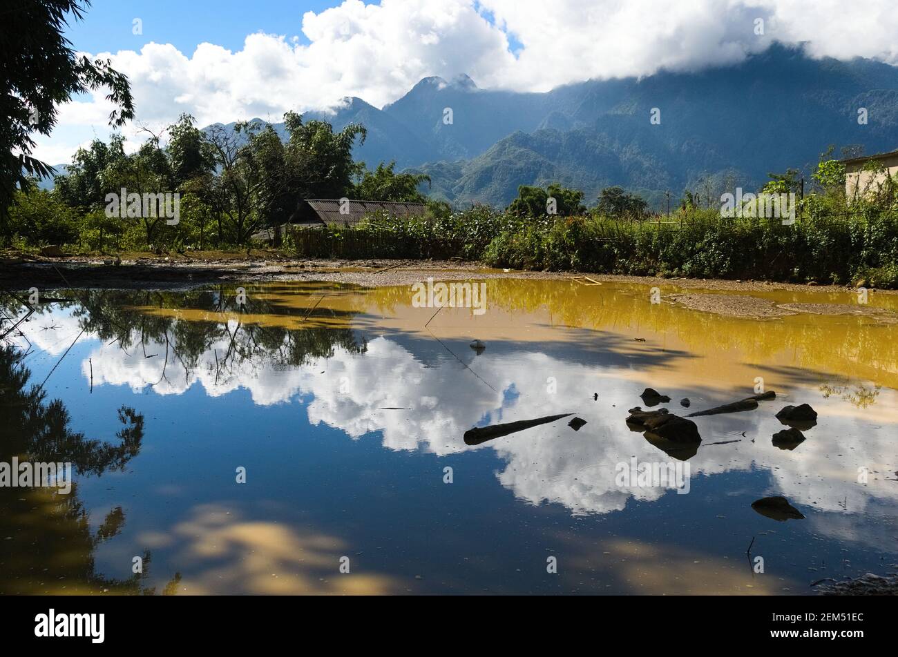 Wolkiger Himmel spiegelt sich im Wasser in einem kleinen Teich in einem kleinen Dorf in den Bergen in der Nähe von Sa Pa, Vietnam Stockfoto