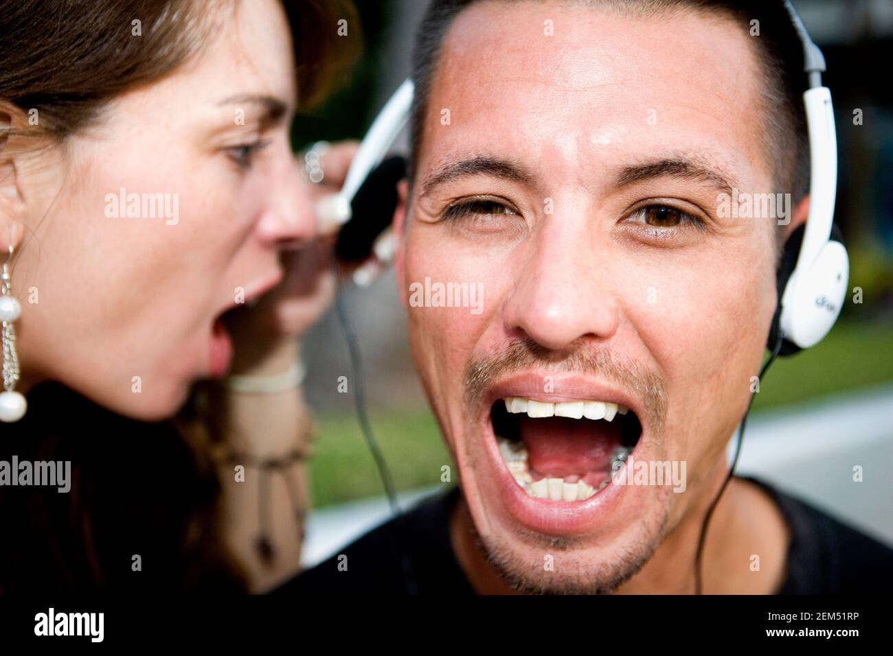 Frau mit mittlerem Erwachsenen, die einem Mann mit mittlerem Erwachsenenalter ins Ohr schreit Kopfhörer tragen Stockfoto