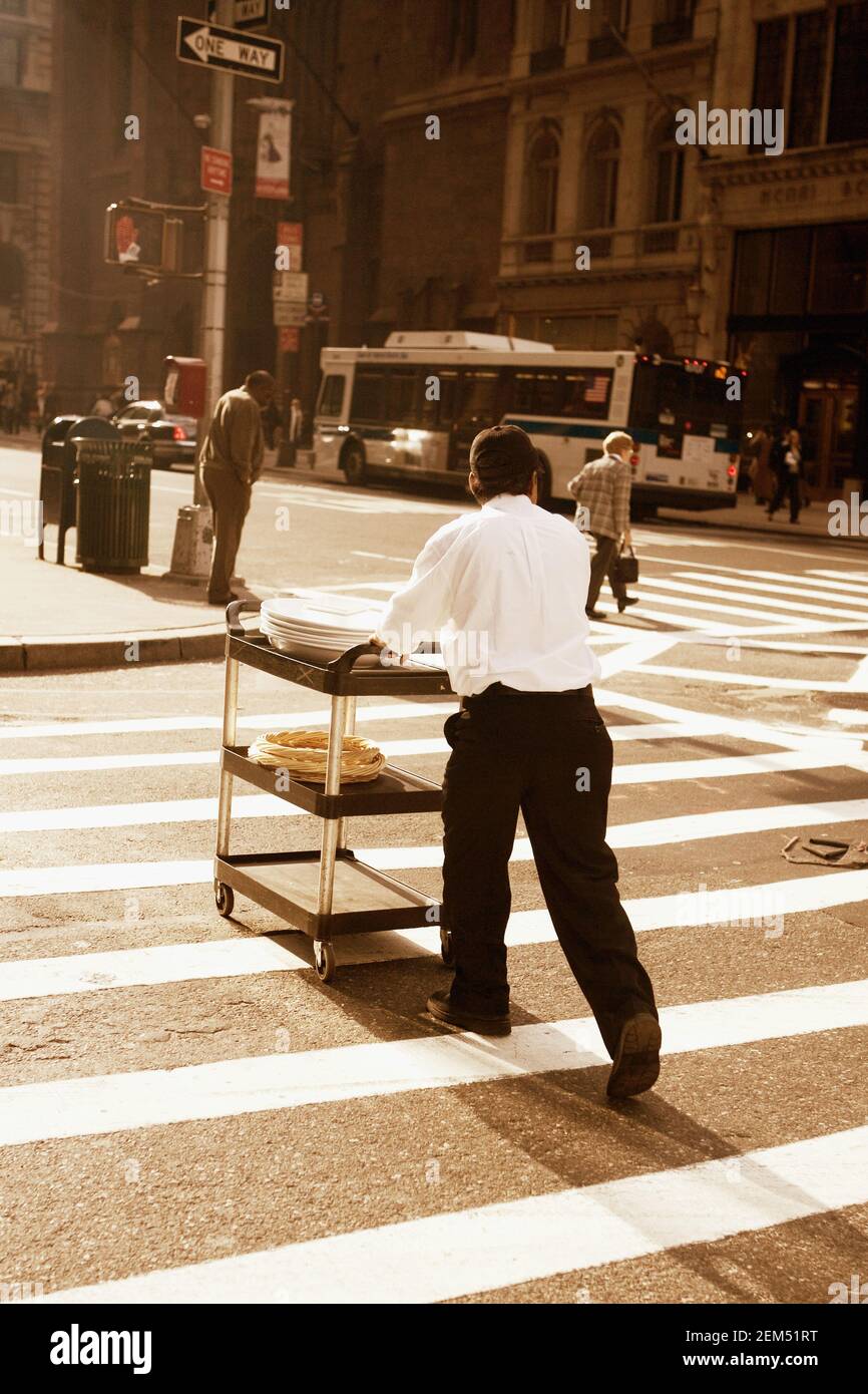Rückansicht eines Kellners, der einen Servierwagen auf der Straße schiebt, New York City, New York State, USA Stockfoto