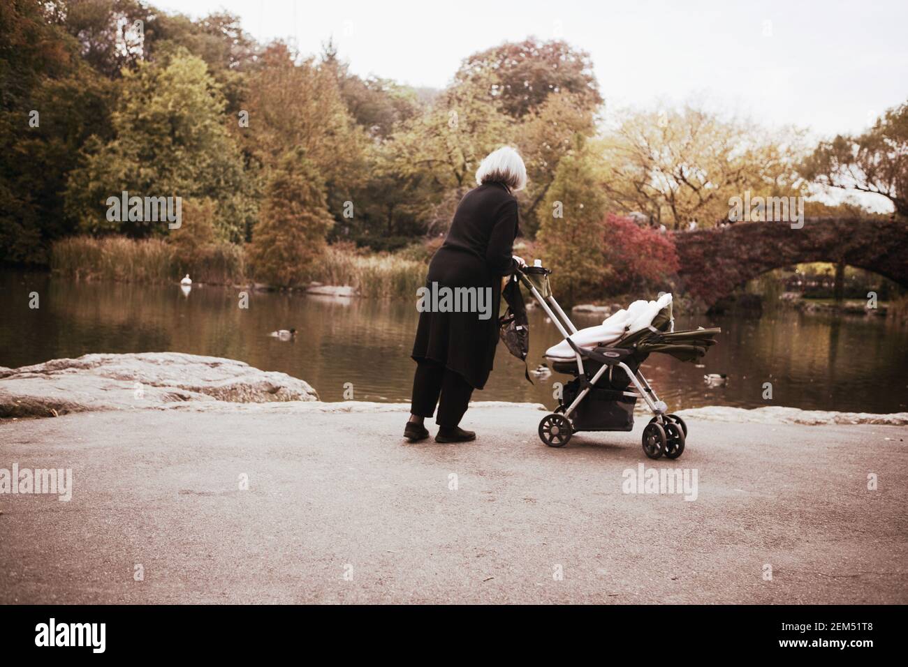 Rückansicht einer Frau, die am Flussufer einen Kinderwagen schiebt, New York City, New York State, USA Stockfoto