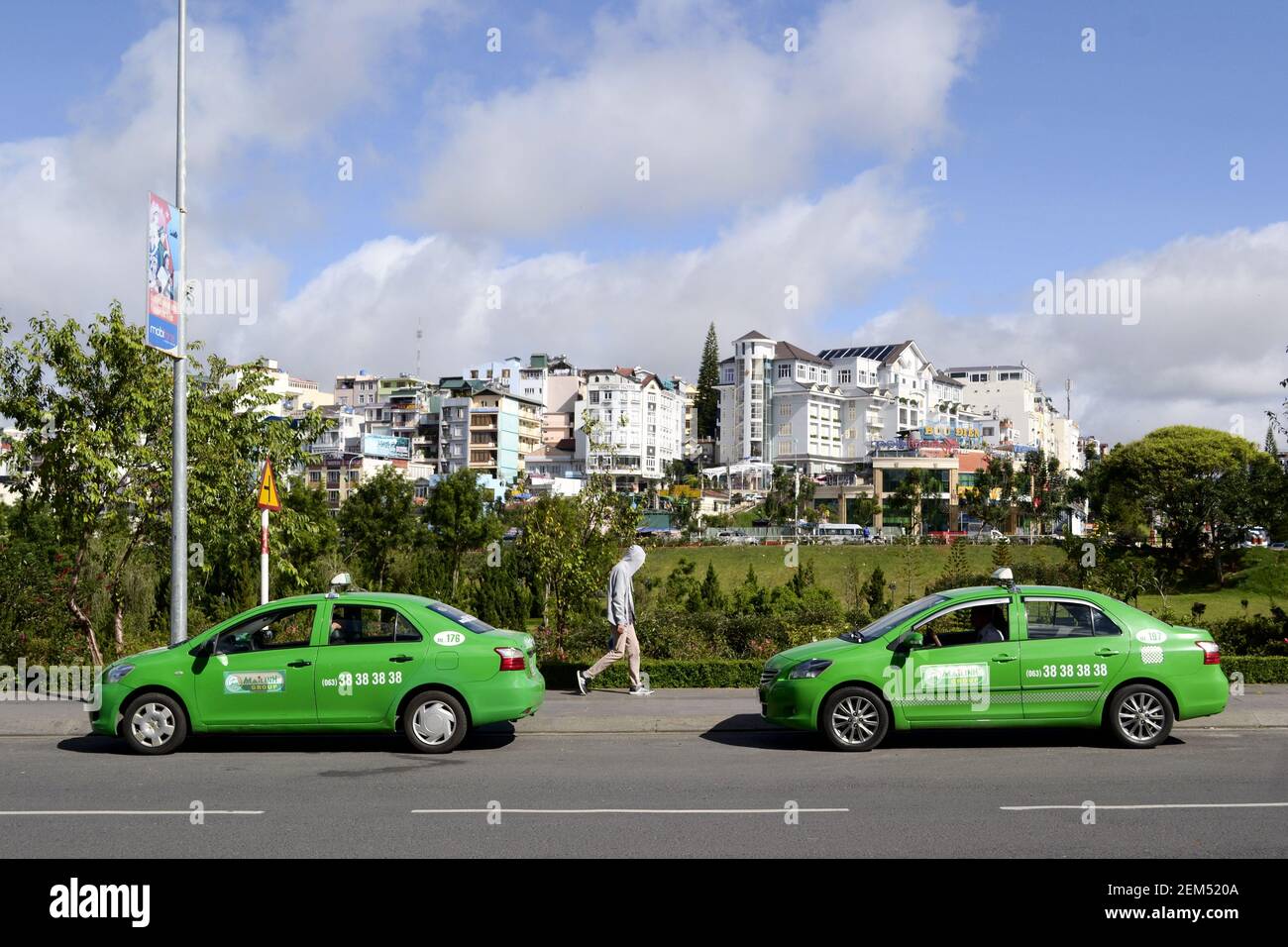 Da Lat, Vietnam - Juli 2015: Zwei ähnliche grüne Taxiwagen auf der Straße und Mann, der zwischen ihnen läuft. Grünes Farbkonzept. Seitenansicht Stockfoto