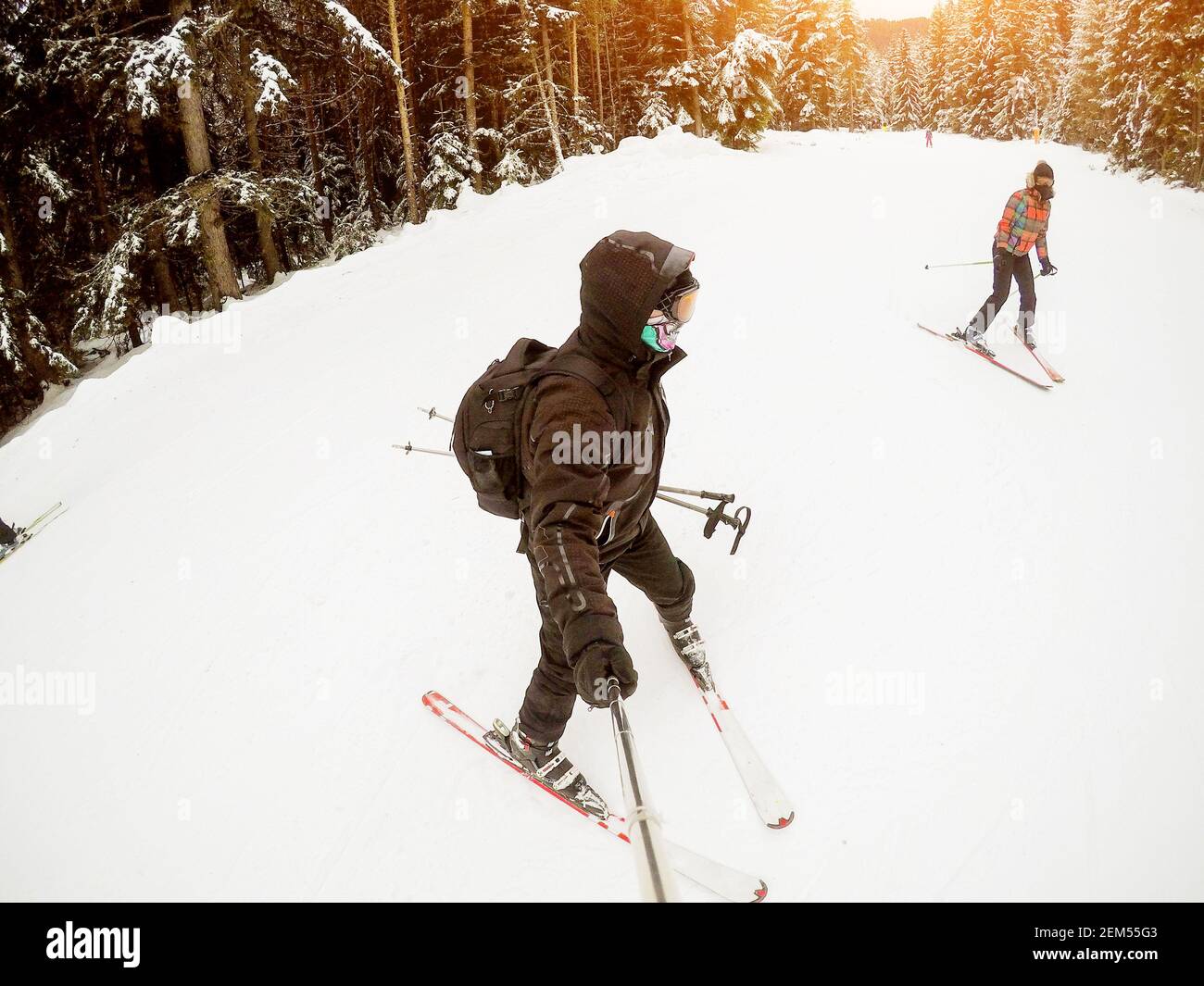 Mann im Skianzug erfassen einen schönen Moment mit einem attraktiven Mädchen im Hintergrund im Wald beim Skifahren. Stockfoto