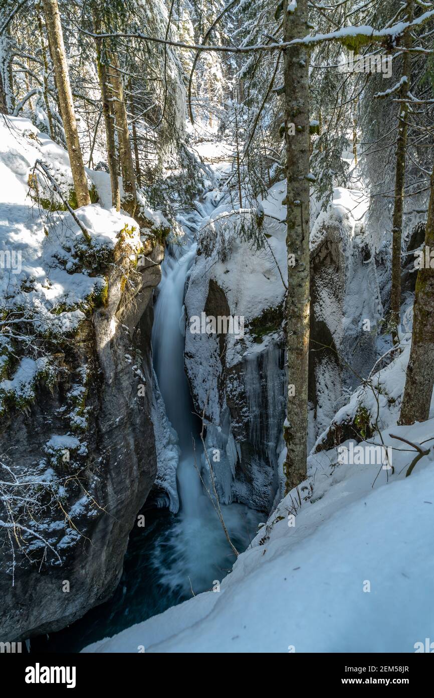 Winter im Bregenzerwald mit vereistem Bach im verschneiten Wald. Winter im Bregenzerwald mit eisigem Bach im verschneiten Wald. Wasserfall und Sonne Stockfoto