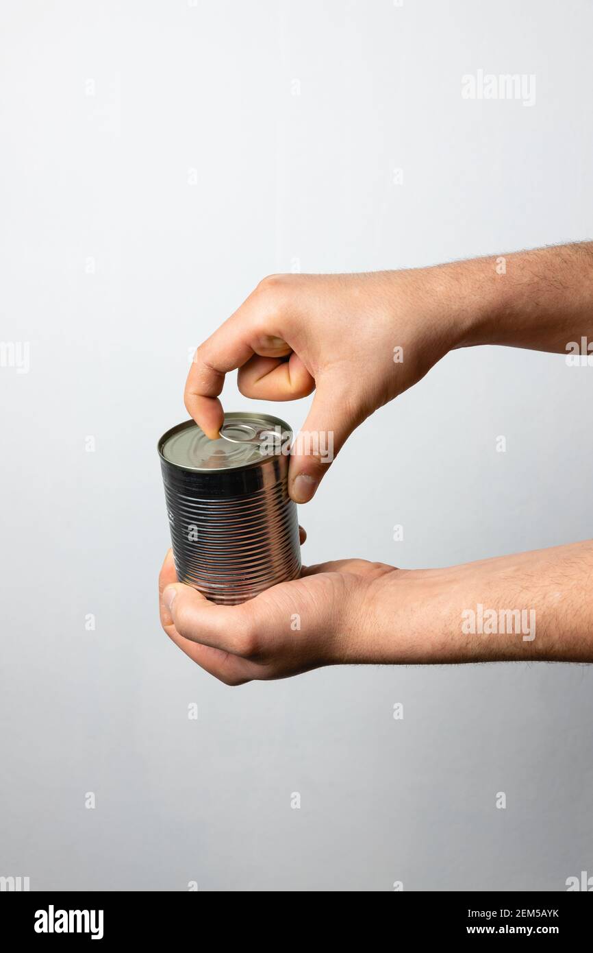 Die Hände des Mannes öffnen eine AluminiumDose voller Nahrung. Recycling von Materialien, ökologisch. Aluminium ist endlos recycelbar Stockfoto